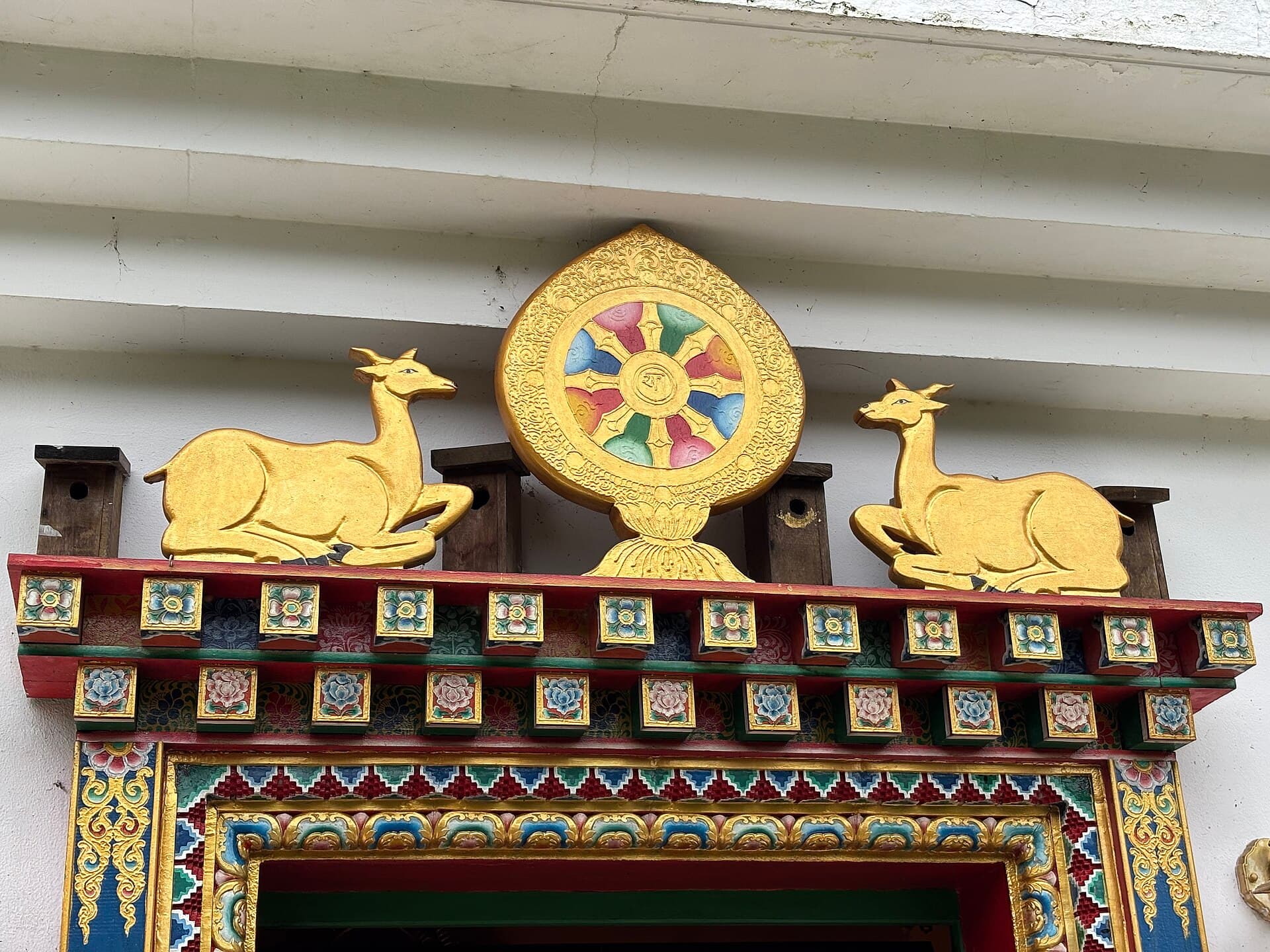 Gilded eight-spoked dharma wheel flanked by two deer above a monastery entrance