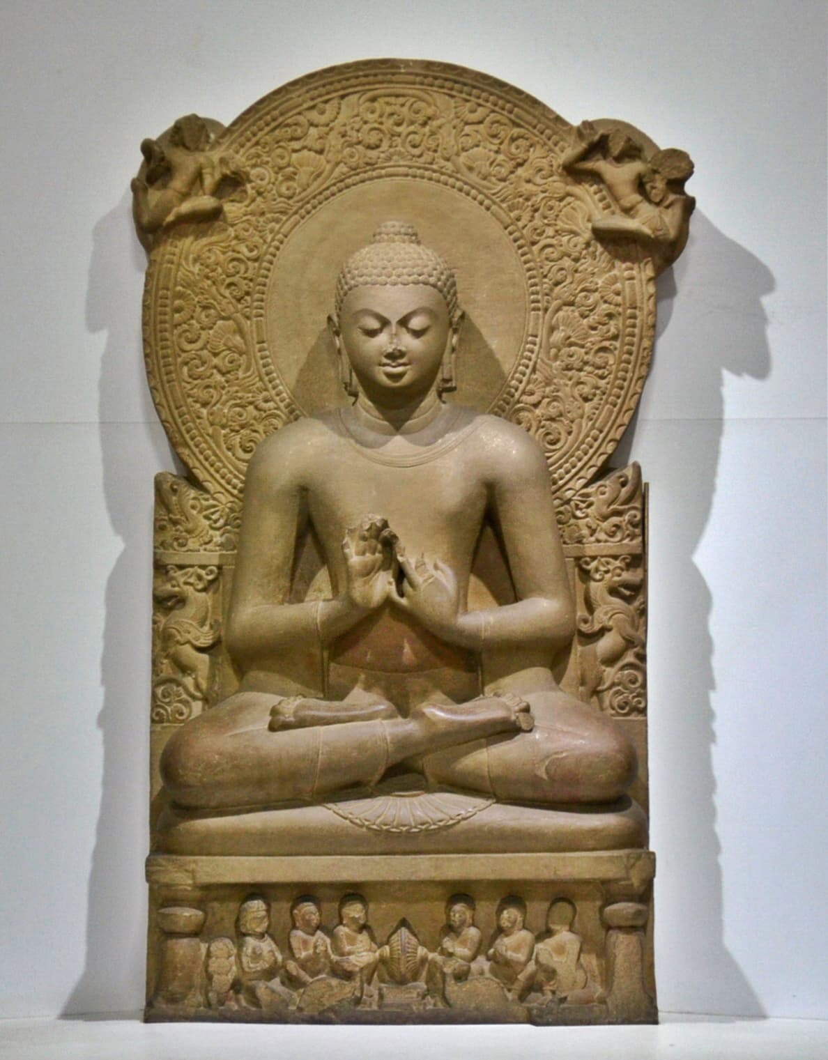 Seated stone Buddha image in meditation (dhyana mudra), flanked by an ornately carved halo and donor figures