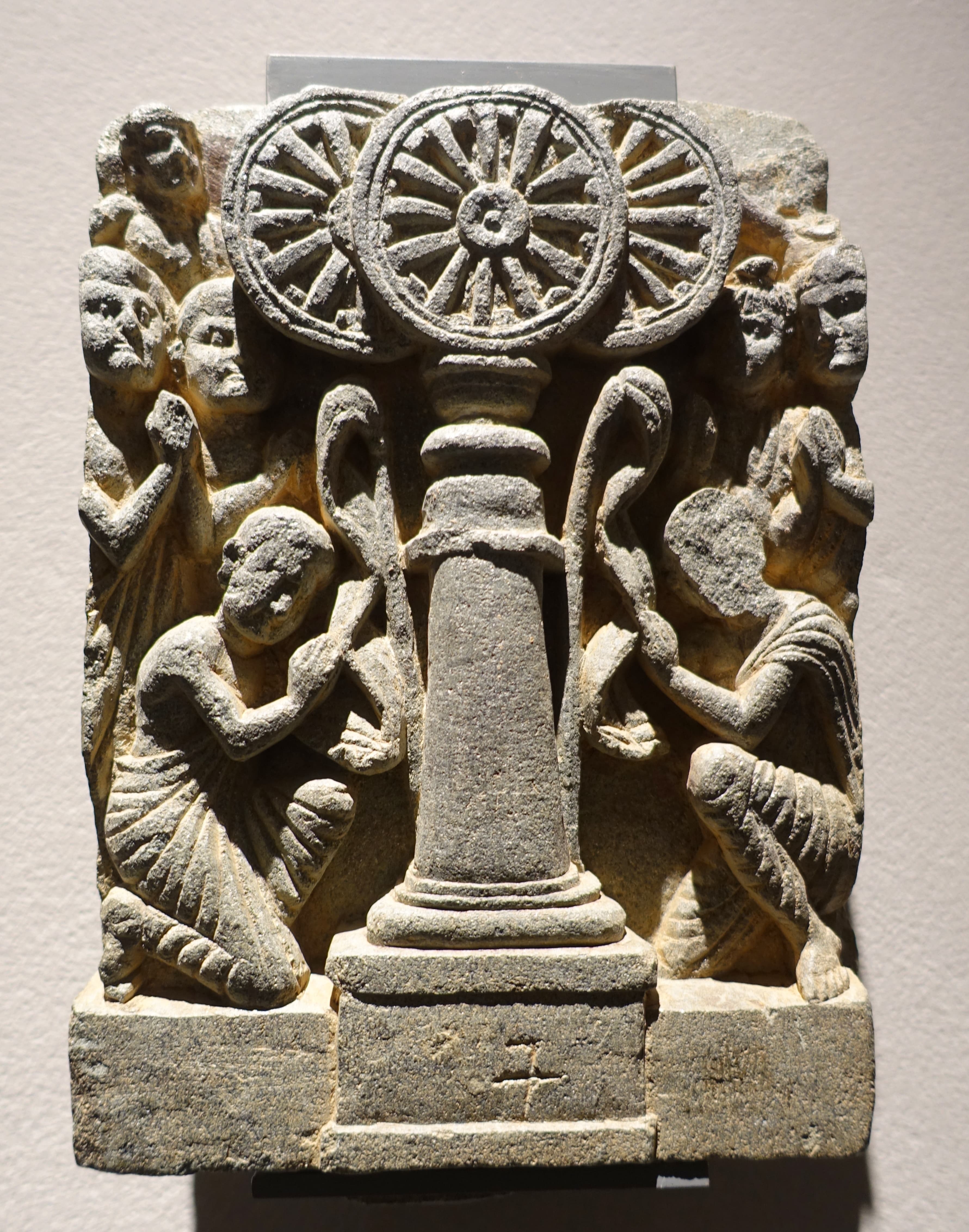 Ancient Gandharan stone relief of devotees venerating dharma wheels on pillars, an aniconic-era depiction of the triratna