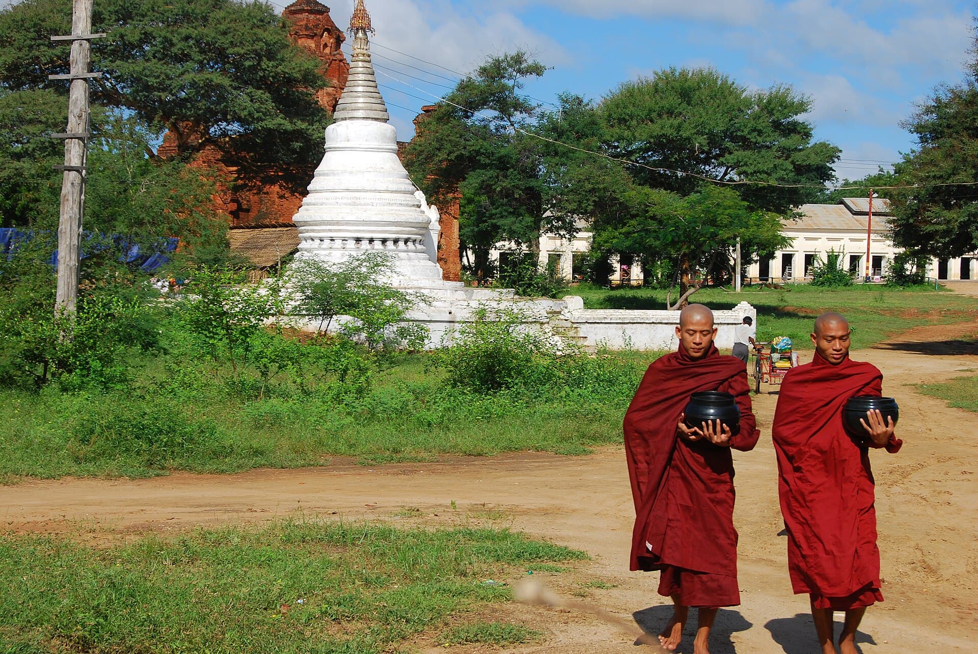 Monks walking the road past a whitewashed stupa on alms round