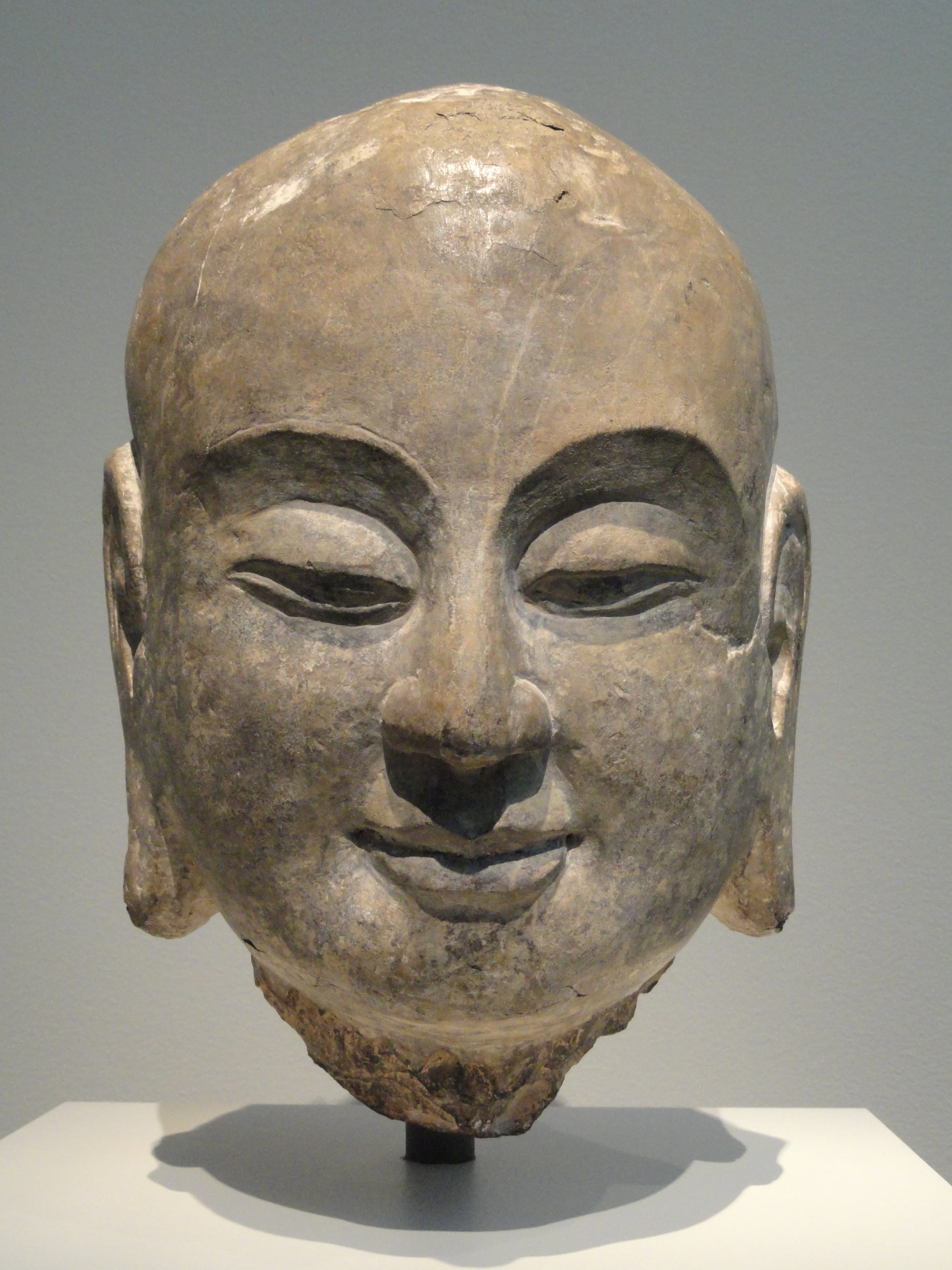 Carved stone head of the monk Ananda, serene expression, elongated earlobes, from a museum collection