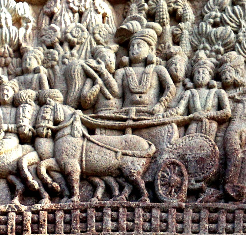 Ancient stone relief carving showing a royal figure, identified as Emperor Ashoka, riding in a horse-drawn chariot with attendants
