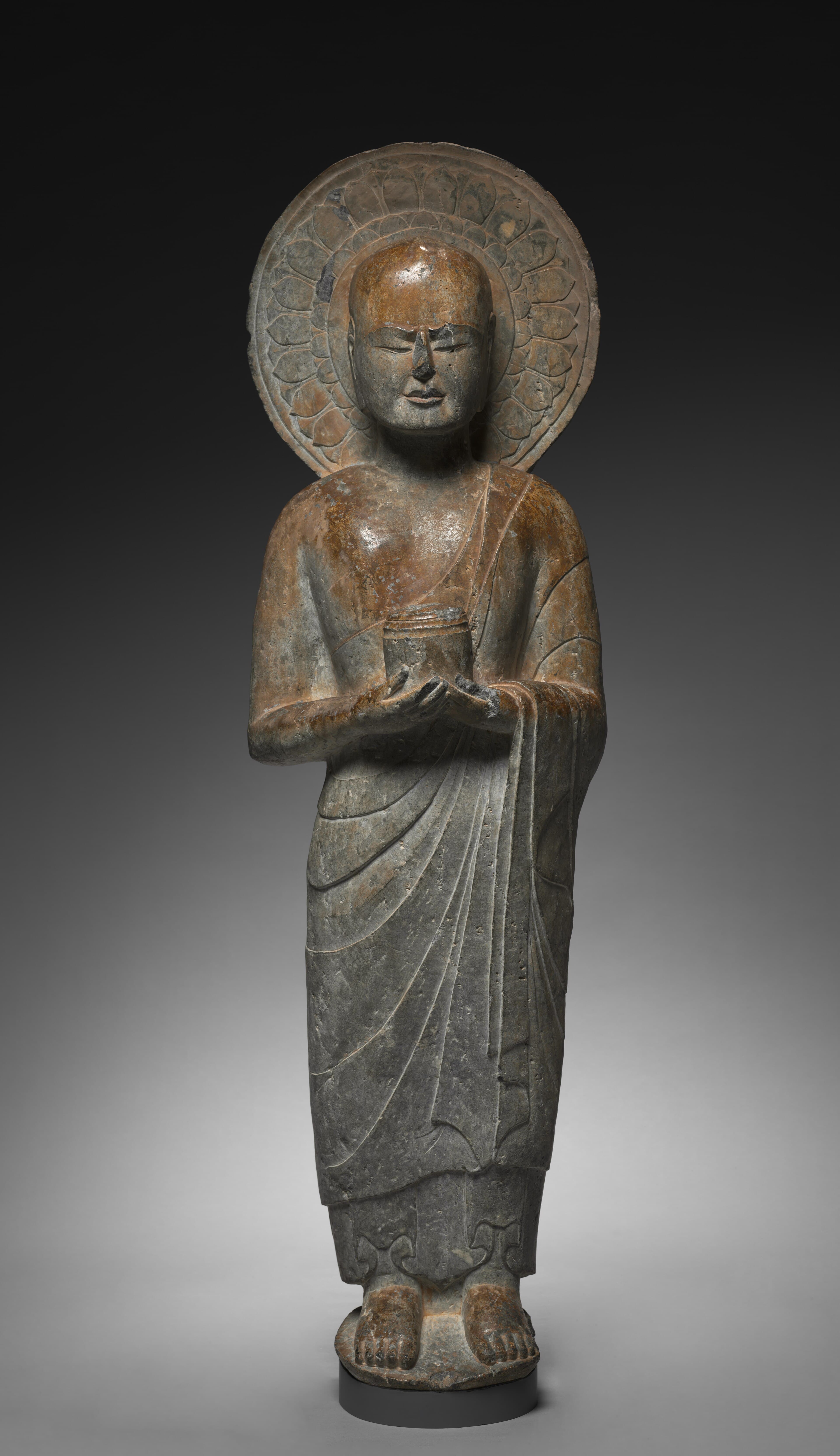 Stone relief sculpture of a standing arhat holding an alms bowl, identified as Mahakassapa, with an elaborate carved halo behind his head